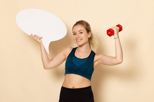 Free photo front view young female in sport outfit holding dumbbells and white speech bubble