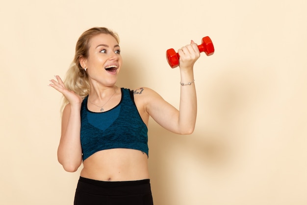 Front view young female in sport outfit holding red dumbbells on a light white wall sport body health beauty workout