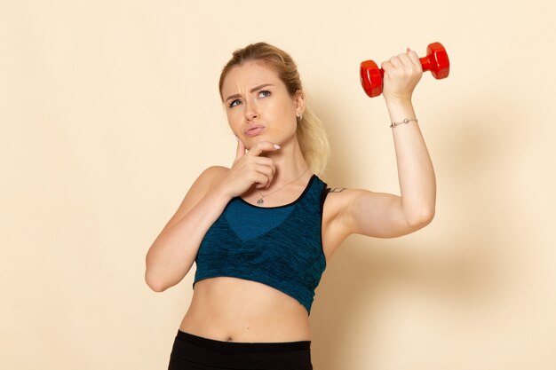 Front view young female in sport outfit holding red dumbbells and thinking on white wall sport body health beauty workout