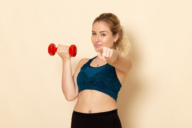 Front view young female in sport outfit holding red dumbbells on the white wall health sport body beauty workout