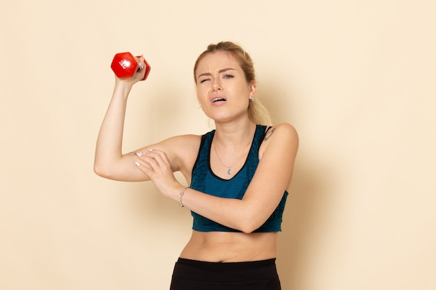 Front view young female in sport outfit holding red dumbbells on the white wall sport body health beauty workout woman