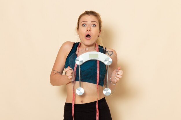 Front view young female in sport outfit holding scales on white wall fit body sport beauty health exercise