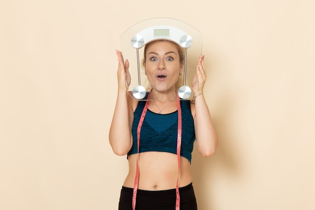 front view young female in sport outfit holding scales on a white wall fit body sport beauty health exercises