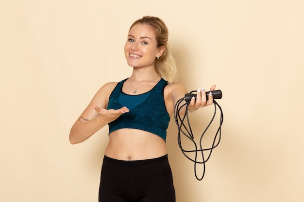 Front view young female in sport outfit holding skipping ropes on a light white wall health beauty workout body sport