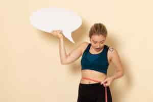 Free photo front view young female in sport outfit holding white sign and measuring her body