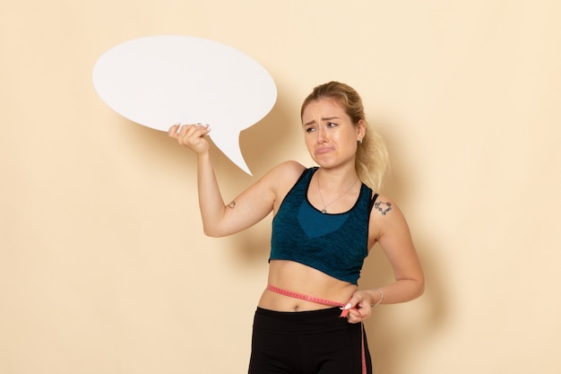 Front view young female in sport outfit holding white sign and measuring her body