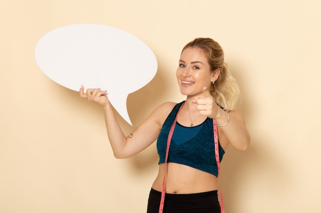 Foto gratuita giovane femmina di vista frontale in attrezzatura di sport che tiene segno bianco e sorridere