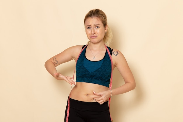 Foto gratuita giovane femmina di vista frontale in attrezzatura sportiva che misura il suo corpo triste a causa del suo peso