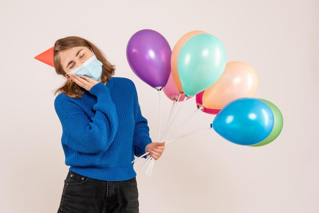 フロントビュー無菌マスクをかぶった若い女性が色とりどりの風船を握っています