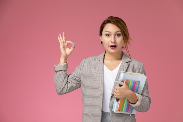 Front view young female student in grey coat with copybooks on pink background lessons university college study