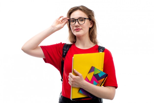 A front view young female student in red shirt black bag holding copybooks files smiling on the white