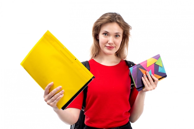 A front view young female student in red shirt black bag holding copybooks files smiling on the white