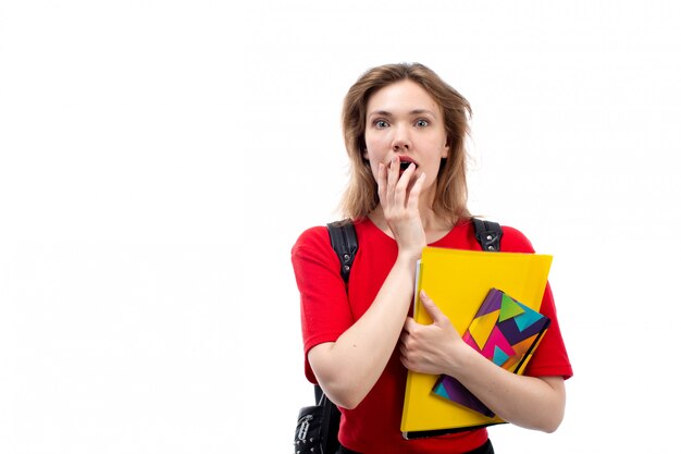 A front view young female student in red shirt black bag holding copybooks shocked expression on the white