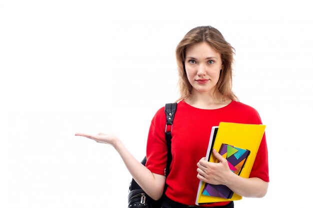 A front view young female student in red shirt black bag holding pen and copybooks on the white