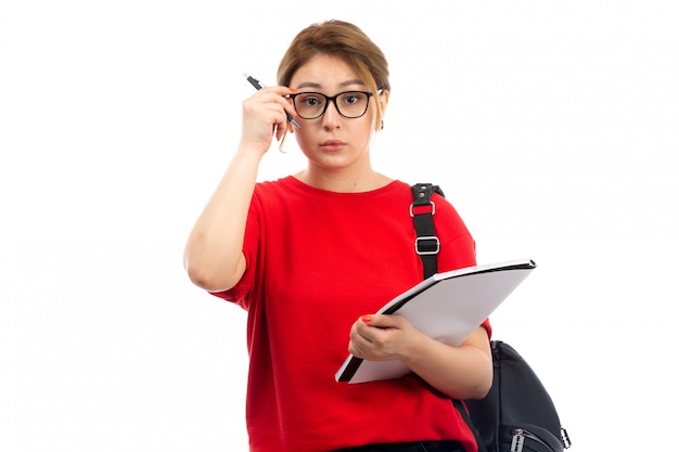 白のコピーブックを保持している赤いtシャツブラックジーンズの正面の若い女子学生