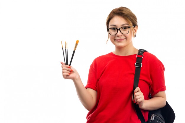 白に笑みを浮かべて絵筆を保持している赤いtシャツブラックジーンズの正面の若い女子学生