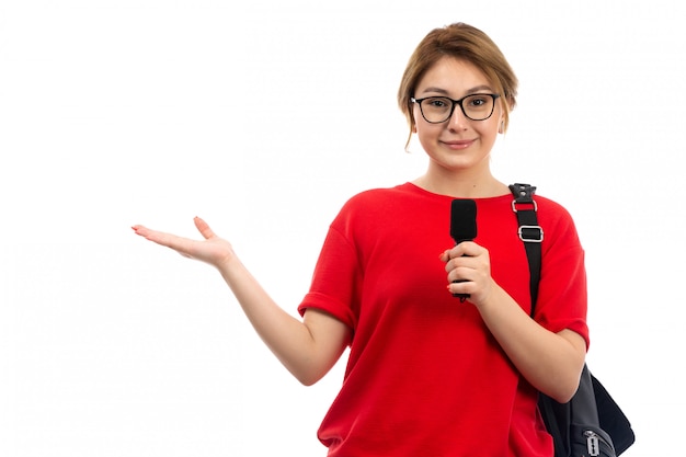 白に笑みを浮かべてマイクを持っている黒いバッグを着ている赤いtシャツの正面の若い女子学生