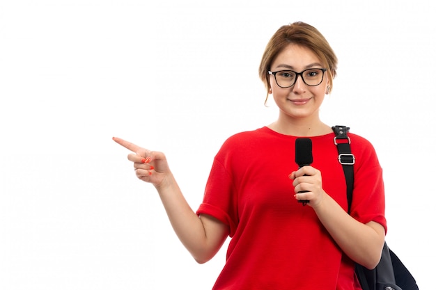 A front view young female student in red t-shirt wearing black bag holding microphone smiling on the white