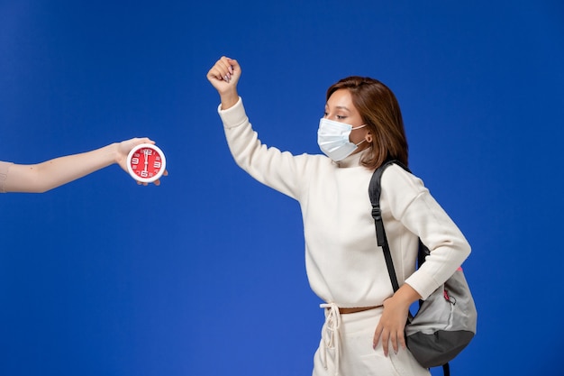 Front view young female student in white jersey wearing mask and bag on blue wall