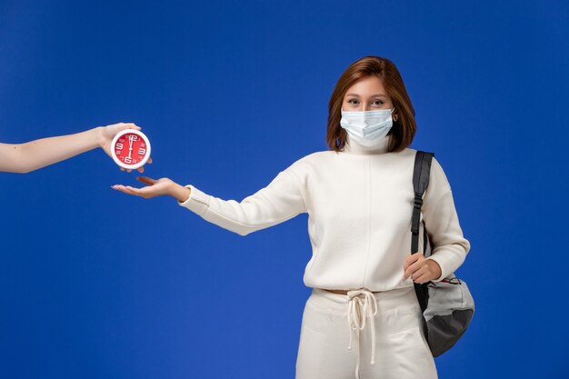 Front view young female student in white jersey wearing mask and bag on blue wall