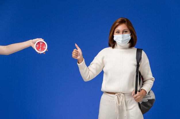Front view young female student in white jersey wearing mask and bag posing on blue wall
