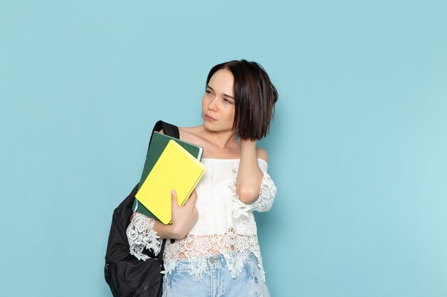 白いシャツのブルージーンズと青い空間の女子学生にコピーブックを保持している黒いバッグの正面の若い女子学生