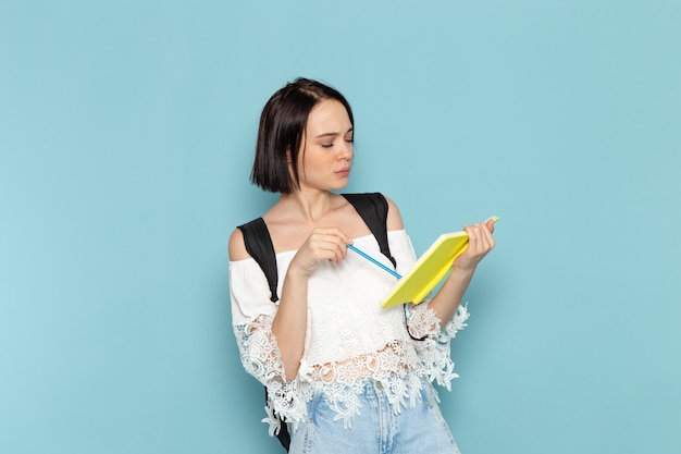 Front view of young female student in white shirt blue jeans and black bag writing notes