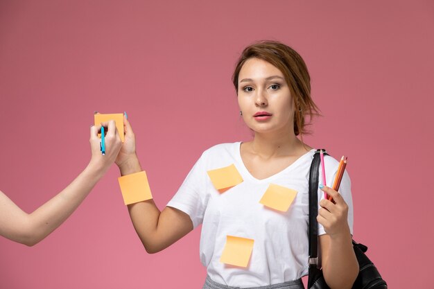 분홍색 배경 학생 수업 대학 대학에 연필로 포즈 흰색 t- 셔츠와 회색 바지에 전면보기 젊은 여성 학생