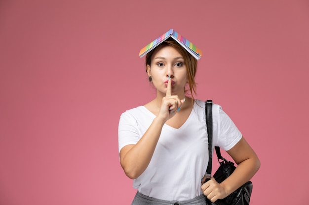 ピンクの机の上の彼女の頭にコピーブックと白いTシャツと灰色のズボンの正面図若い女子学生学生レッスン大学