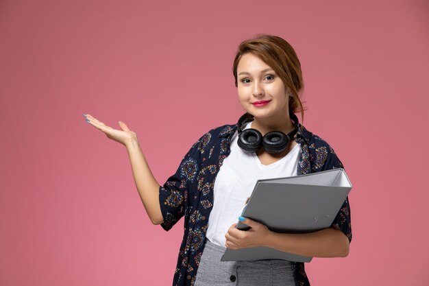 Front view young female student in white t-shirt and grey trousers with grey document in her hands on the pink background student lessons university college