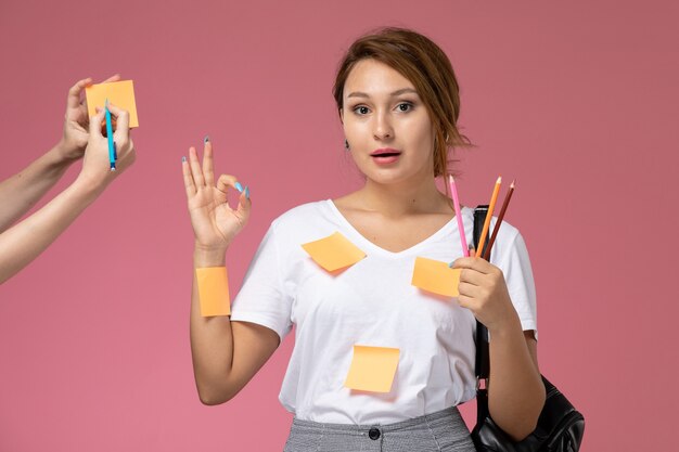 분홍색 배경 수업 대학 대학 연구에 연필을 들고 흰색 티셔츠에 전면보기 젊은 여성 학생