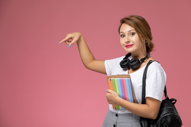 ピンクの背景にコピーブックを持って笑っている白いTシャツの正面図若い女子学生レッスン大学大学研究書