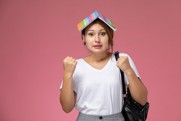 Front view young female student in white t-shirt with copybook and delighted expression on pink background lesson university college study book