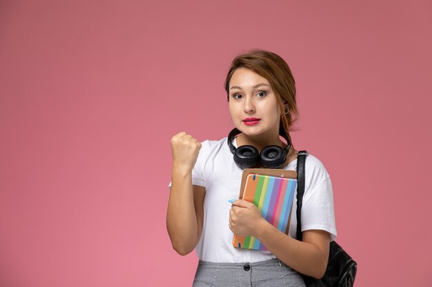 法帖イヤホンとピンクの背景でポーズをとるバッグと白いTシャツの正面図若い女子学生レッスン大学大学研究書