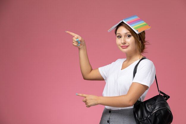 コピーブックとピンクの背景に笑顔の白いTシャツの正面図若い女子学生レッスン大学大学研究書