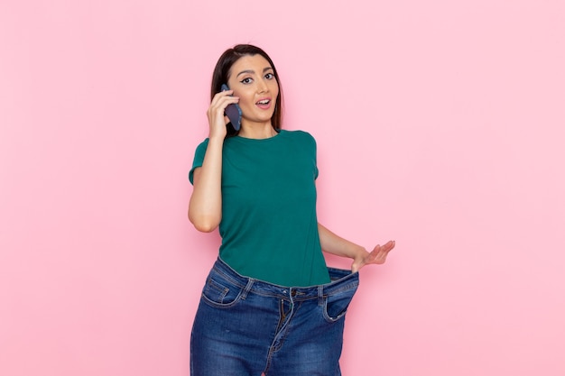 ピンクの壁のエクササイズスポーツトレーニングアスリートウエストの美しさで電話で話している正面図若い女性