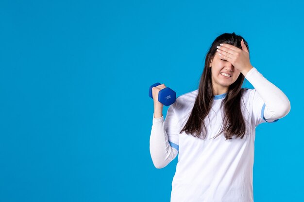 青い壁にダンベルで運動するのにうんざりしている正面図若い女性