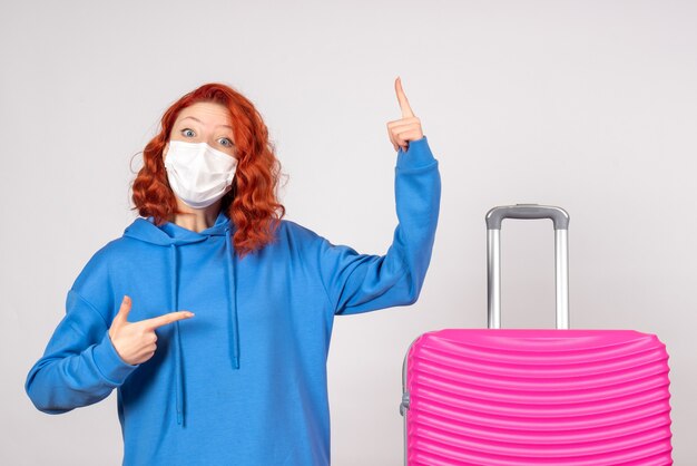 Front view of young female tourist with pink bag in mask on the white wall