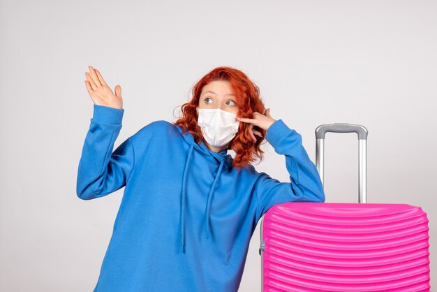 Front view of young female tourist with pink bag in mask on white wall