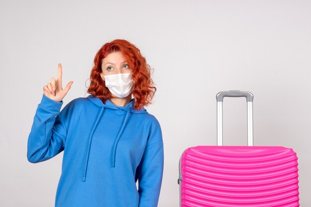 Front view of young female tourist with pink bag in mask on white wall