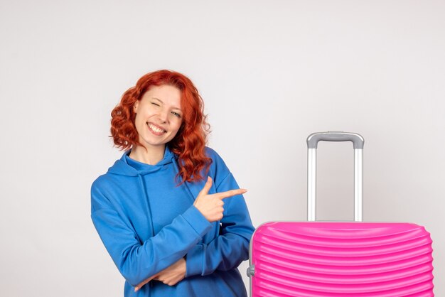 Front view of young female tourist with pink bag on white wall