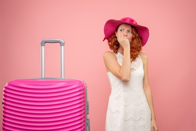 Front view of young female tourist with pink hat and bag nervous on pink wall