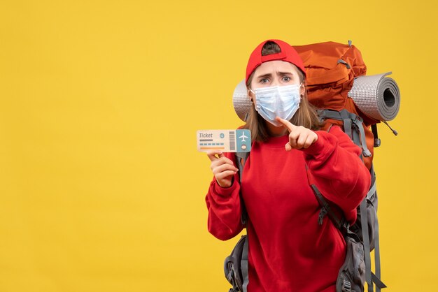 Front view young female traveler with backpack and mask holding ticket pointing finger up