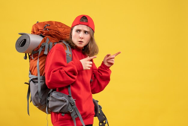 Молодая женщина-путешественница с рюкзаком, указывая пальцем вправо, вид спереди