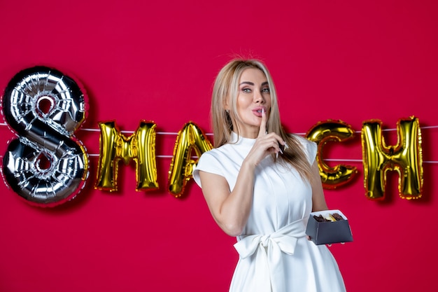 Front view young female in white dress holding chocolate candies on decorated red womens day holiday color