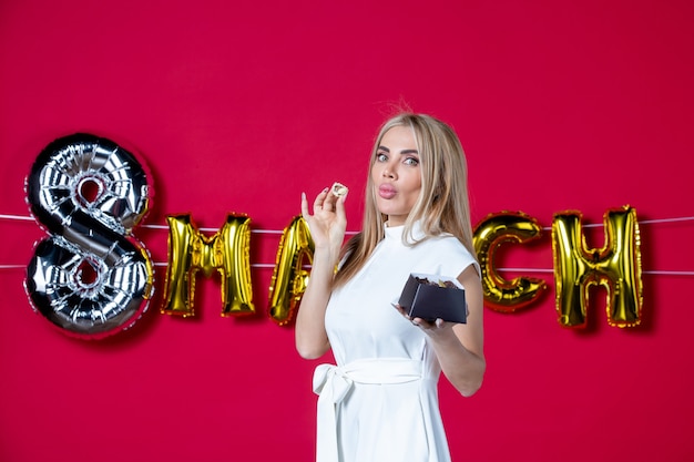 Free photo front view young female in white dress posing with delicious candies on decorated red womens day