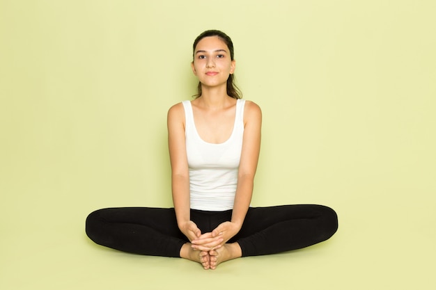 Foto gratuita una giovane femmina di vista frontale in camicia bianca e pantaloni neri che propongono che si siedono nella posa di yoga di meditazione