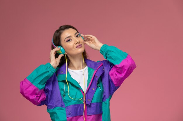 Front view young female in white shirt colored coat listening to music on pink wall, photo color woman pose model