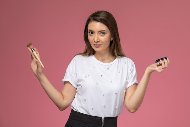 Free photo front view young female in white shirt doing her make-up on light-pink wall