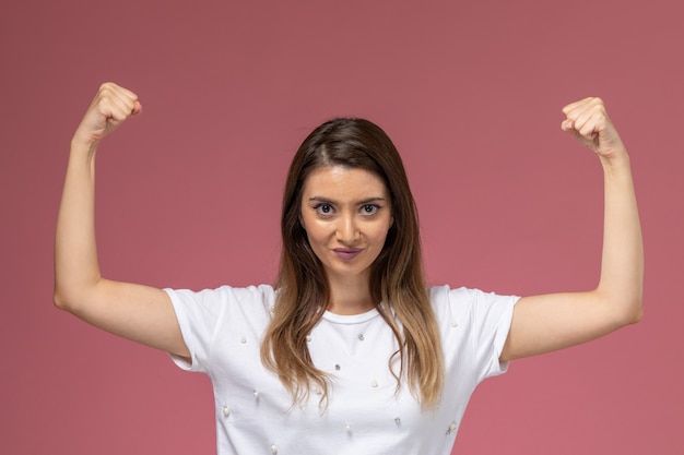 Front view young female in white shirt flexing on pink wall